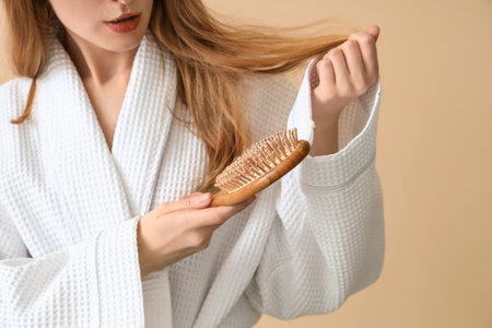 Young woman with hair loss problem brushing on beige background, closeupの写真素材