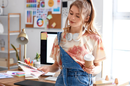 Female graphic designer with cup of coffee and color palettes in officeの写真素材