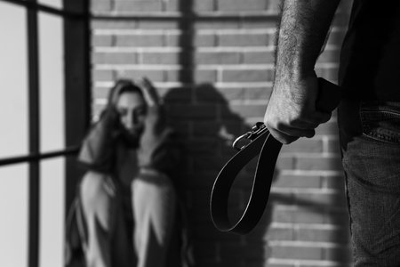 Young man with belt and his scared wife at home, closeup. domestic violence conceptの写真素材