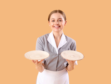 Beautiful young waitress with empty plates on beige backgroundの写真素材