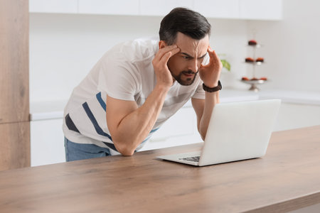 Young man with laptop having panic attack in the kitchenの写真素材
