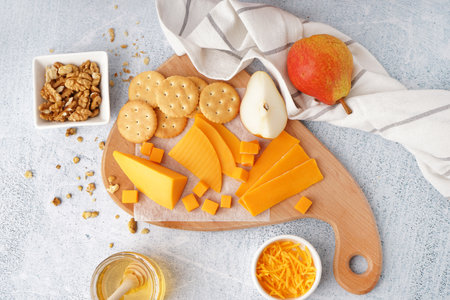 Board with tasty cheddar cheese, crackers, pear, nuts and honey on light backgroundの写真素材