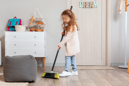 Cute little girl sweeping floor with broom at homeの写真素材
