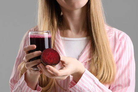 Young woman with glass of vegetable juice and beet on gray background, closeupの写真素材