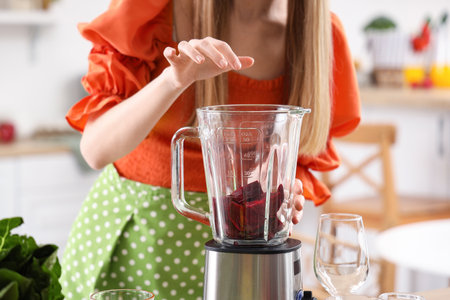 Young woman putting cut beet into blender in kitchen, closeupの写真素材