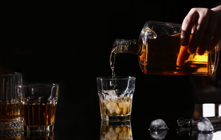 Woman pouring tasty rum from bottle into glasses on dark backgroundの写真素材