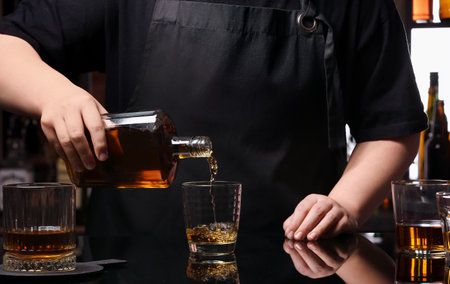 Woman pouring tasty rum from bottle into glasses at table in bar, closeupの写真素材
