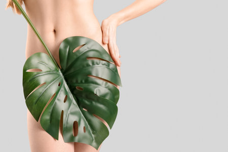 Naked young woman with tropical leaf on light background. Epilation conceptの写真素材