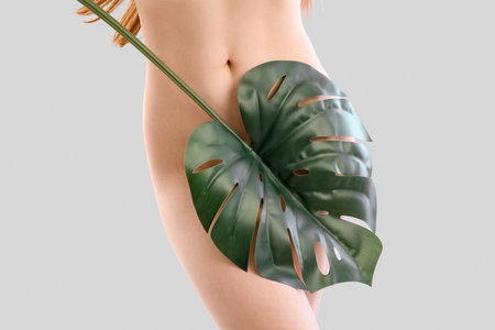 Naked young woman with tropical leaf on light background. Epilation conceptの写真素材
