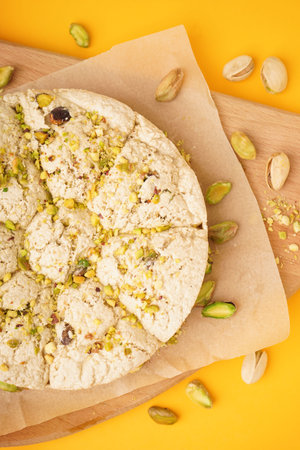 Wooden board of tasty Tahini halva with pistachios on yellow background, closeup
