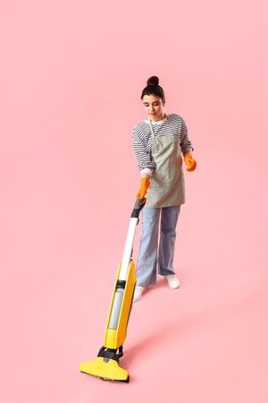 Young woman with vacuum cleaner on pink backgroundの写真素材