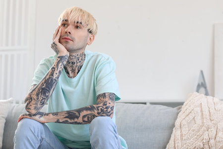Young tattooed man sitting on sofa at homeの写真素材