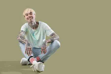 Tattooed young man sitting on green background