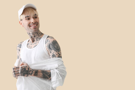 Tattooed young man in cap on beige backgroundの写真素材
