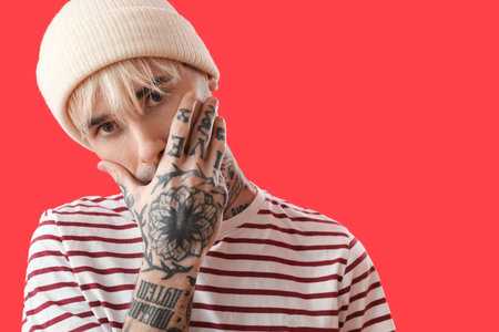Tattooed young man in hat on red background, closeupの写真素材