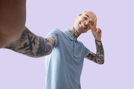 Tattooed young man taking selfie on lilac backgroundの写真素材