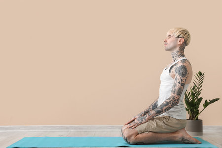 Tattooed young man meditating near beige wallの写真素材