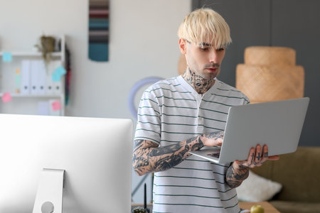 Tattooed graphic designer working with laptop in officeの写真素材