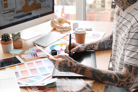 Tattooed graphic designer working with tablet and paint palette on table in office, closeupの写真素材