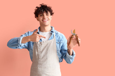 Male gardener pointing at secateurs on pink background