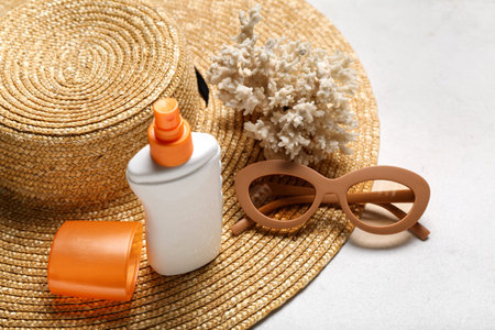Bottle of sunscreen cream, hat, sunglasses and coral on light background, closeup. melanoma concept