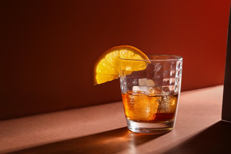 Glass of rum with ice cubes and orange slice on brown backgroundの写真素材