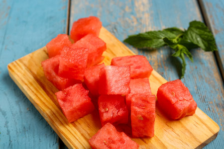 Board with pieces of fresh watermelon and mint on blue wooden backgroundの写真素材