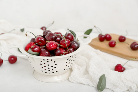 Colander and board with sweet cherries on white backgroundの写真素材