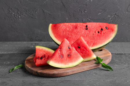 Board with pieces of fresh watermelon and mint on black wooden tableの写真素材