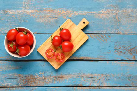 Board and bowl with fresh cherry tomatoes on blue wooden backgroundの写真素材
