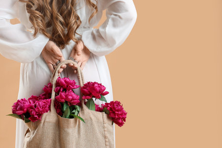 Young woman with eco bag and peony flowers on beige background, back viewの写真素材