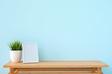 Wooden table with houseplant and blank frame near blue wallの写真素材