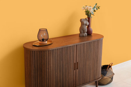 Stylish wooden chest of drawers with decor near orange wall in room