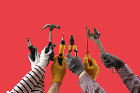 Female hands holding different construction tools on red backgroundの写真素材