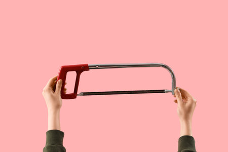 Female hands holding hacksaw on pink backgroundの写真素材