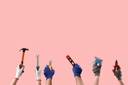 Female and male hands holding different construction tools on pink backgroundの写真素材