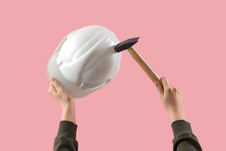 Female hands holding safety hardhat and hammer on pink backgroundの写真素材