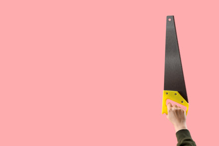Female hand holding handsaw on pink backgroundの写真素材