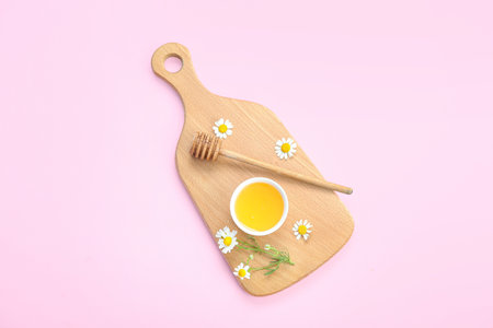 Wooden board with bowl of honey and chamomile flowers on pink backgroundの写真素材