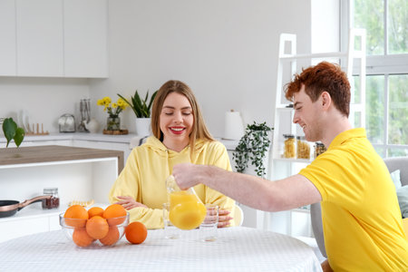 Young man pouring orange juice for his girlfriend in kitchenの写真素材