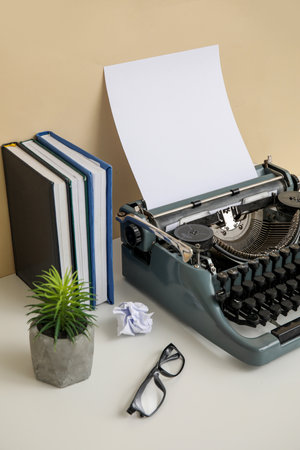Vintage typewriter with books, houseplant and eyeglasses on table near beige wallの写真素材