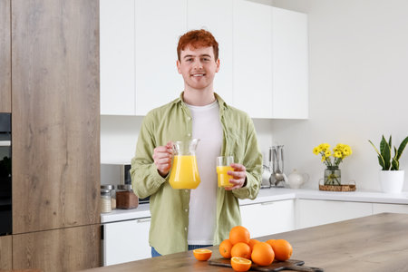 Young man with glass and jug of orange juice in the kitchenの写真素材