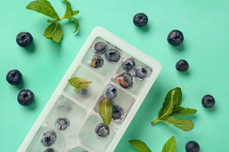 Ice tray with fresh blueberry frozen in ice and mint on blue backgroundの写真素材