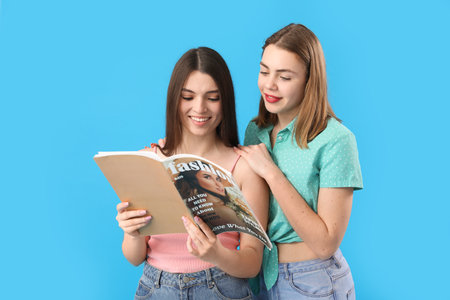 Female friends reading magazine on blue backgroundの写真素材