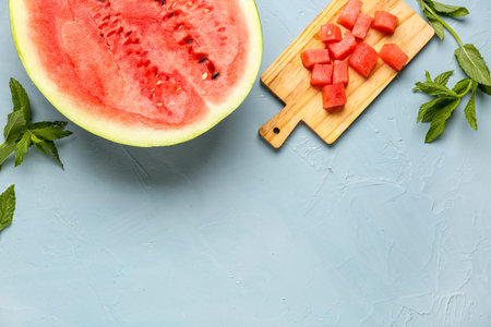 Half of fresh watermelon and board with pieces on blue background