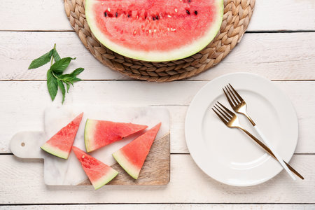 Half of fresh watermelon and board with pieces on white wooden backgroundの写真素材