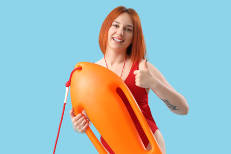 Female lifeguard with rescue buoy showing thumb-up on blue backgroundの写真素材