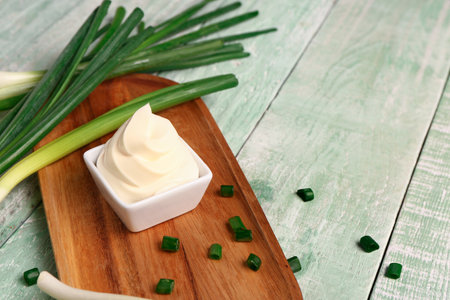 Board with bowl of tasty sour cream and scallion on green wooden backgroundの写真素材