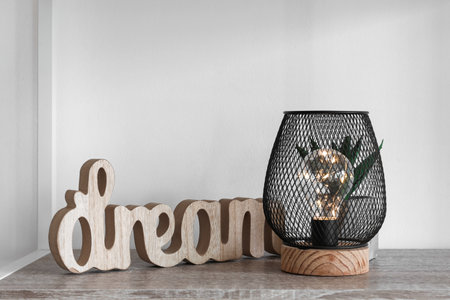 Glowing lamp with decor on shelf near light wallの写真素材