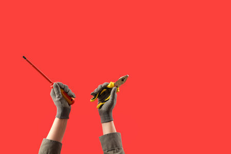 Female hands in gloves holding screwdriver and pliers on red background